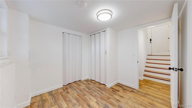 unfurnished room featuring light wood-type flooring, stairs, baseboards, and a textured ceiling