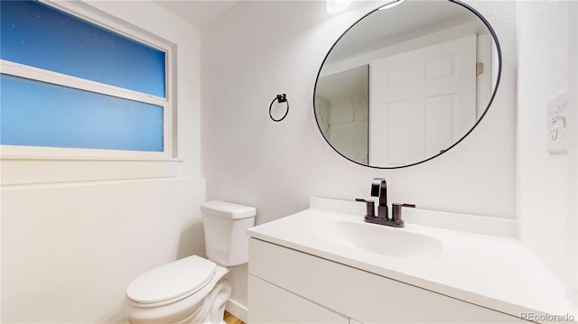 half bathroom featuring toilet, a textured wall, and vanity