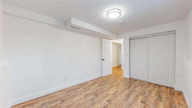 unfurnished bedroom featuring light wood finished floors, baseboards, and a closet