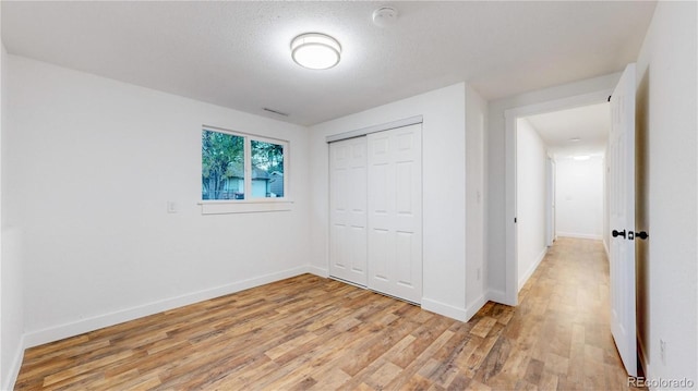 unfurnished bedroom with light wood finished floors, a textured ceiling, baseboards, and a closet