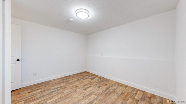 empty room with light wood finished floors, baseboards, and a textured ceiling