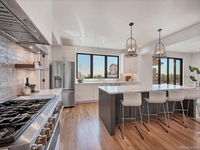 kitchen featuring white cabinetry, high end appliances, light stone countertops, and a spacious island