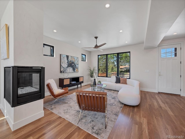 living room with wood-type flooring, a multi sided fireplace, and ceiling fan