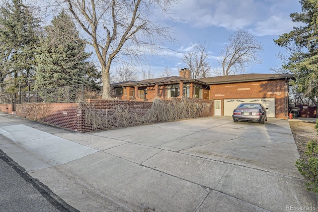 view of front facade with driveway, fence, an attached garage, brick siding, and a chimney