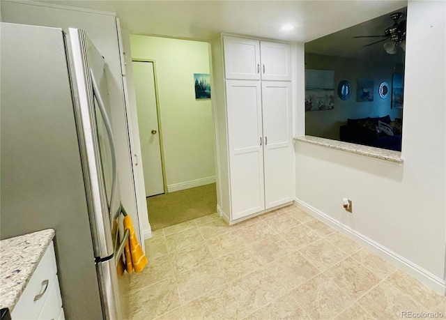 kitchen featuring white cabinetry, stainless steel refrigerator, ceiling fan, and light stone counters