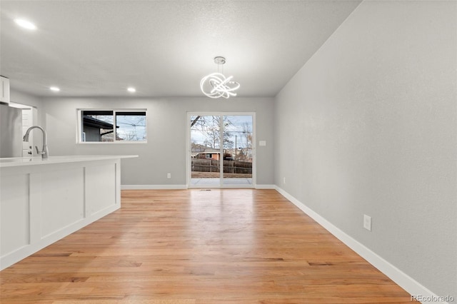 unfurnished dining area with sink, light hardwood / wood-style floors, and a notable chandelier