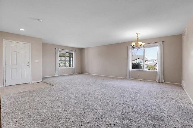 empty room featuring plenty of natural light, light colored carpet, and a notable chandelier