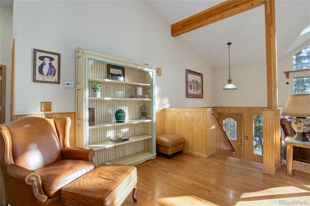 living area with beamed ceiling, high vaulted ceiling, light hardwood / wood-style flooring, and wood walls