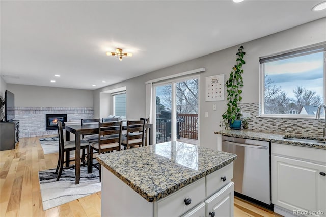 5075 Weeping Willow Cir, Highlands Ranch, CO 80130 - kitchen with dishwasher, a center island, a brick fireplace, light stone counters, and light wood-style floors