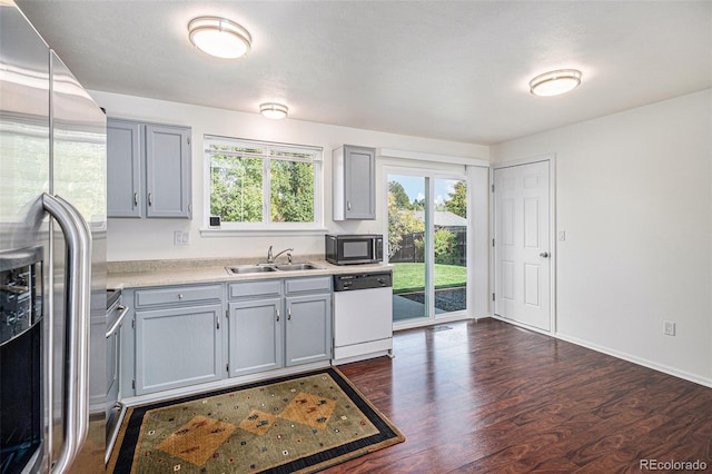 kitchen with appliances with stainless steel finishes, gray cabinetry, sink, and dark hardwood / wood-style flooring