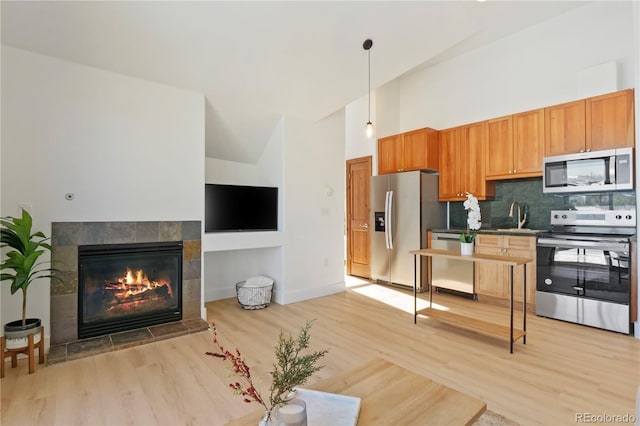 kitchen featuring sink, decorative light fixtures, appliances with stainless steel finishes, a tile fireplace, and light hardwood / wood-style floors