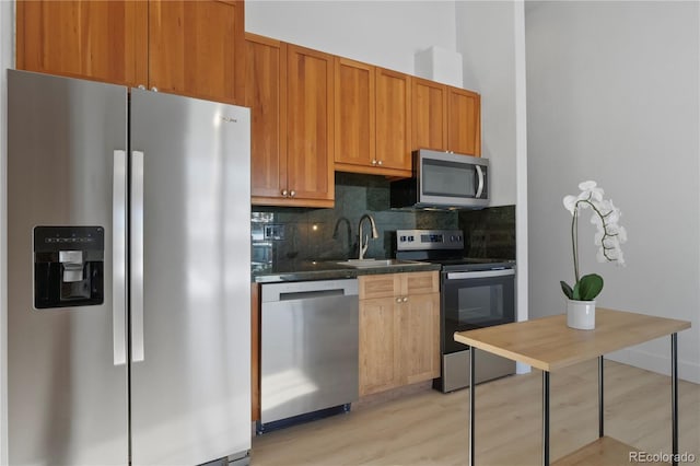 kitchen featuring appliances with stainless steel finishes, sink, light wood-type flooring, and decorative backsplash