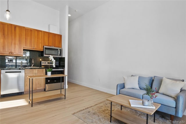 kitchen featuring sink, light hardwood / wood-style flooring, hanging light fixtures, stainless steel appliances, and tasteful backsplash