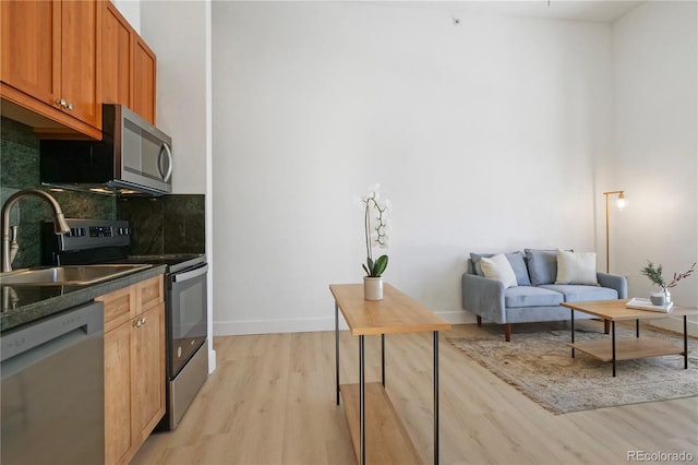 kitchen with stainless steel appliances, sink, decorative backsplash, and light wood-type flooring