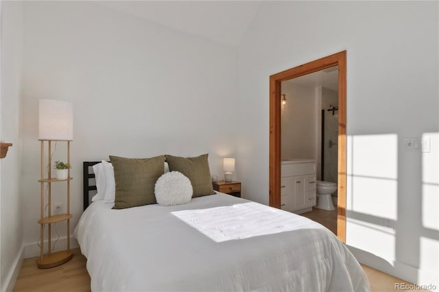 bedroom with ensuite bath, lofted ceiling, and light hardwood / wood-style floors