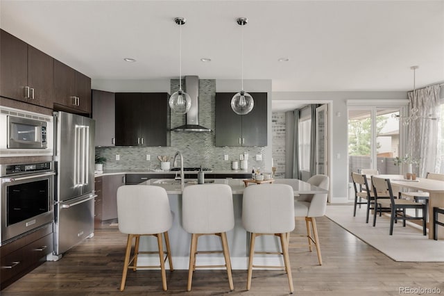 3473 Beeler St, Denver, CO 80238 - kitchen featuring stainless steel appliances, wall chimney exhaust hood, a breakfast bar area, light countertops, and recessed lighting