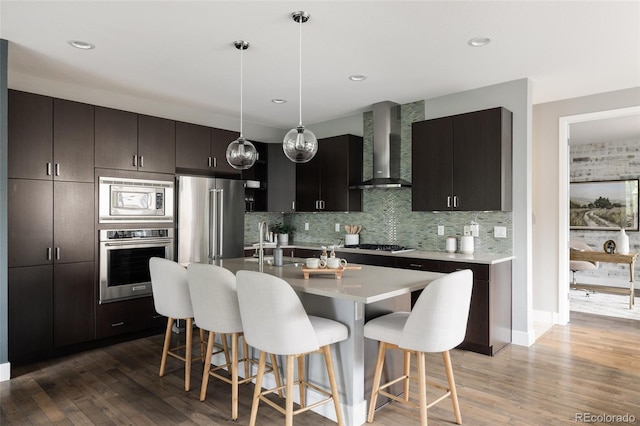 3473 Beeler St, Denver, CO 80238 - kitchen with wall chimney exhaust hood, appliances with stainless steel finishes, a breakfast bar, light wood finished floors, and recessed lighting