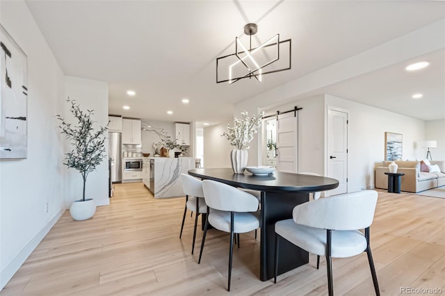 dining area featuring a barn door, light hardwood / wood-style floors, and an inviting chandelier