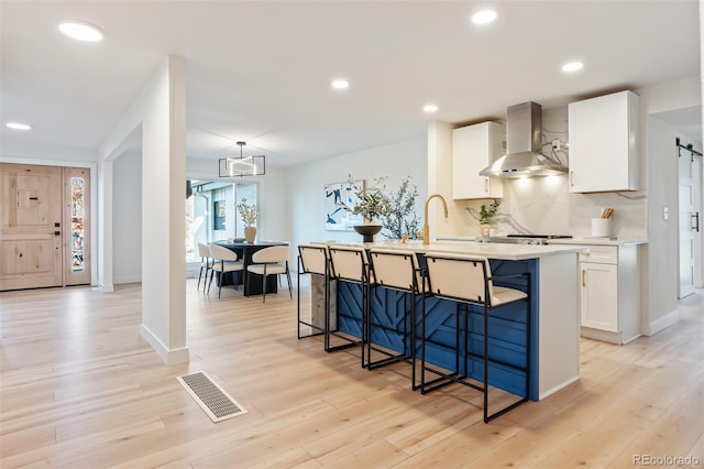 kitchen featuring a barn door, light hardwood / wood-style flooring, white cabinetry, and wall chimney exhaust hood