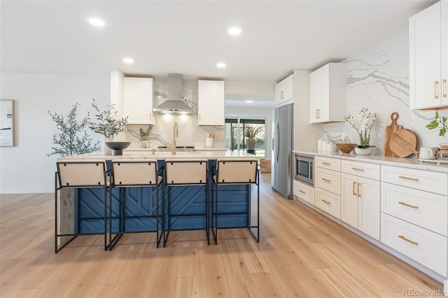 kitchen featuring white cabinets, appliances with stainless steel finishes, light wood-type flooring, and wall chimney range hood