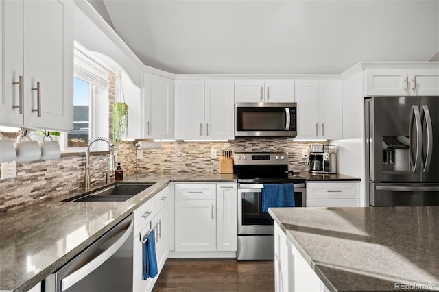 kitchen with appliances with stainless steel finishes, dark stone counters, sink, white cabinets, and tasteful backsplash