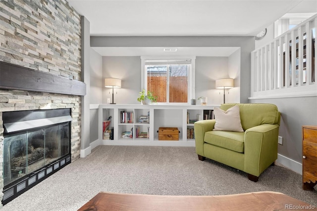 living area with a stone fireplace and carpet floors