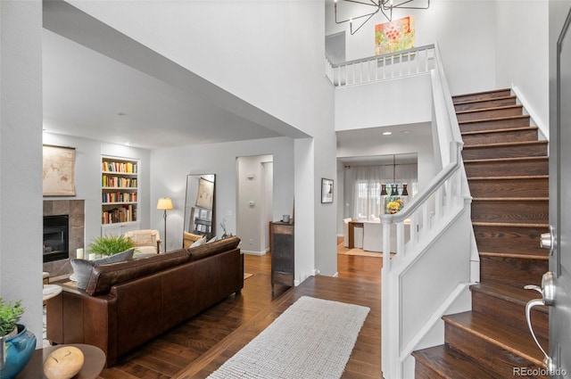 living room featuring a tile fireplace, built in shelves, a chandelier, and dark wood-type flooring