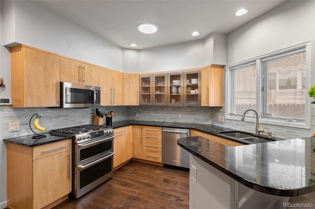 kitchen with sink, dark hardwood / wood-style floors, dark stone countertops, kitchen peninsula, and stainless steel appliances