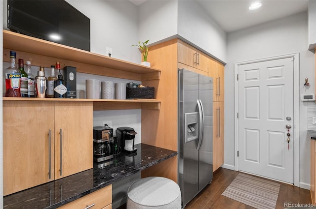 kitchen with dark stone countertops, stainless steel refrigerator with ice dispenser, light brown cabinetry, and dark wood-type flooring