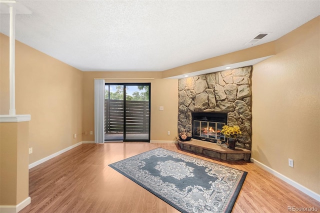 living room with wood-type flooring, a stone fireplace, and a textured ceiling