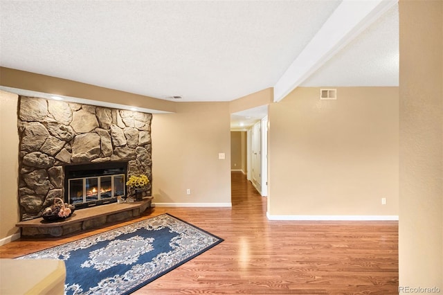 living room with hardwood / wood-style flooring, a stone fireplace, beam ceiling, and a textured ceiling