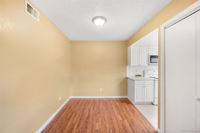 kitchen with white electric range, a textured ceiling, white cabinets, and light wood-type flooring