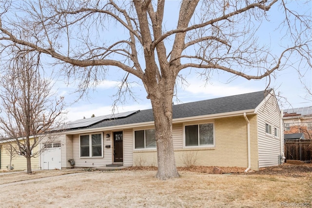 ranch-style home with roof mounted solar panels, brick siding, a shingled roof, and fence