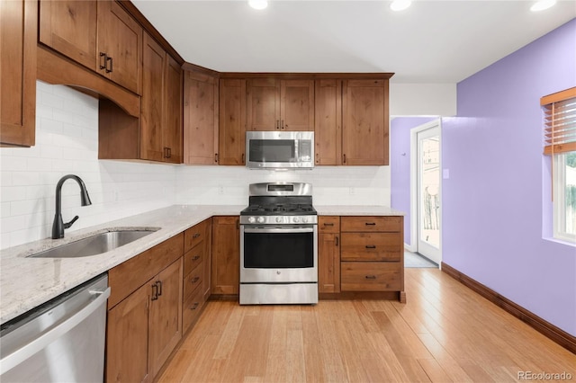 kitchen featuring light stone counters, light wood finished floors, a sink, decorative backsplash, and stainless steel appliances