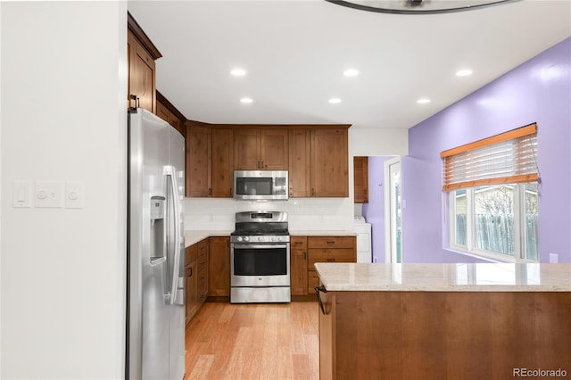 kitchen with light stone countertops, light wood-style flooring, washer / clothes dryer, appliances with stainless steel finishes, and backsplash