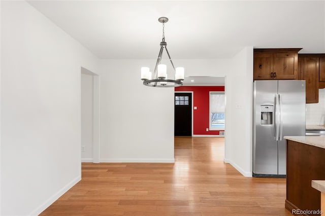 kitchen with an inviting chandelier, stainless steel fridge with ice dispenser, light wood finished floors, decorative backsplash, and hanging light fixtures