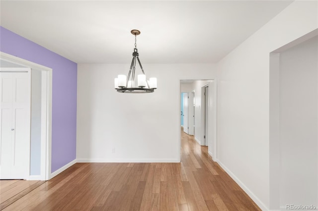 unfurnished dining area featuring light wood-style flooring, baseboards, and a chandelier