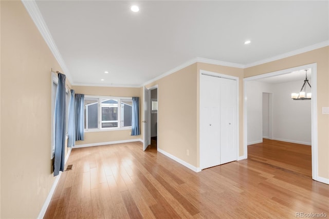 empty room with a chandelier, baseboards, light wood-style floors, and ornamental molding