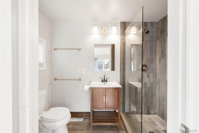 bathroom with wood finished floors, toilet, a stall shower, and vanity