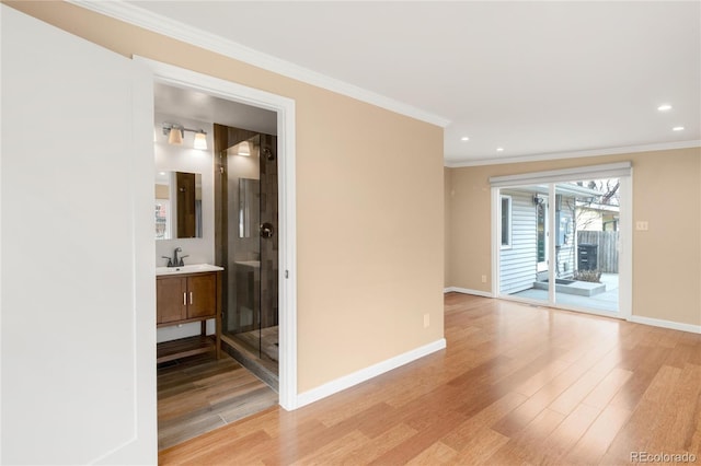 empty room featuring crown molding, baseboards, light wood finished floors, and a sink