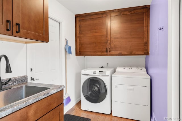 laundry room with baseboards, cabinet space, a sink, washing machine and dryer, and light wood-type flooring