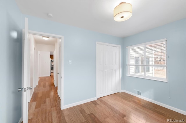 unfurnished bedroom featuring light wood-style flooring, baseboards, visible vents, and a closet