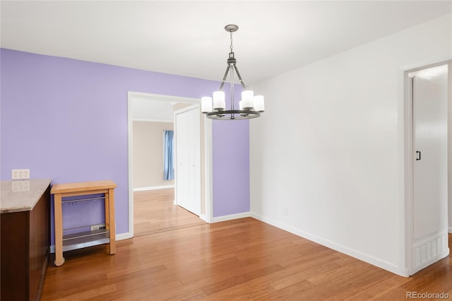 unfurnished dining area with light wood-style flooring, a notable chandelier, and baseboards