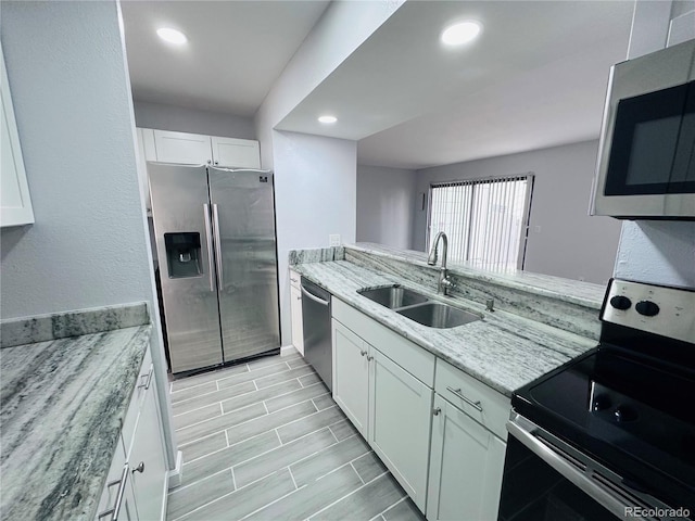 kitchen with light stone counters, recessed lighting, appliances with stainless steel finishes, white cabinetry, and a sink