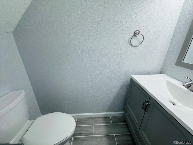 bathroom with baseboards, toilet, vanity, and a textured wall