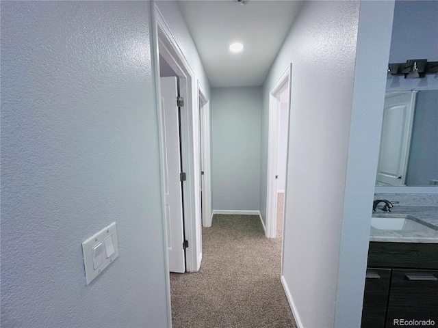 corridor featuring a sink, baseboards, and carpet