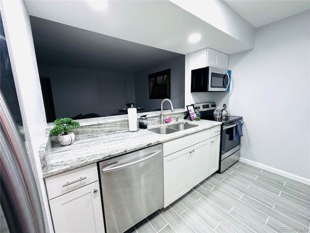 kitchen featuring a sink, baseboards, white cabinetry, light stone counters, and appliances with stainless steel finishes