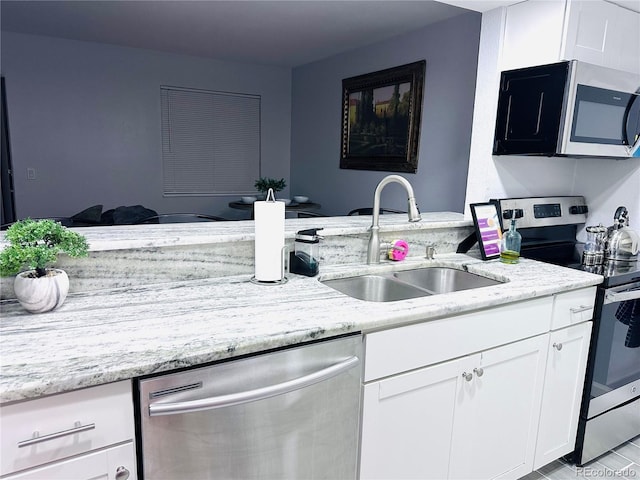 kitchen with white cabinets, stainless steel appliances, a sink, light stone countertops, and a peninsula