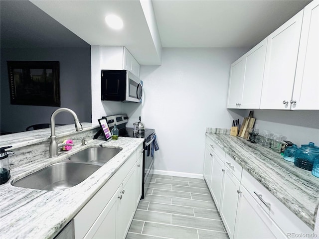 kitchen with stainless steel appliances, a sink, baseboards, white cabinetry, and light stone countertops