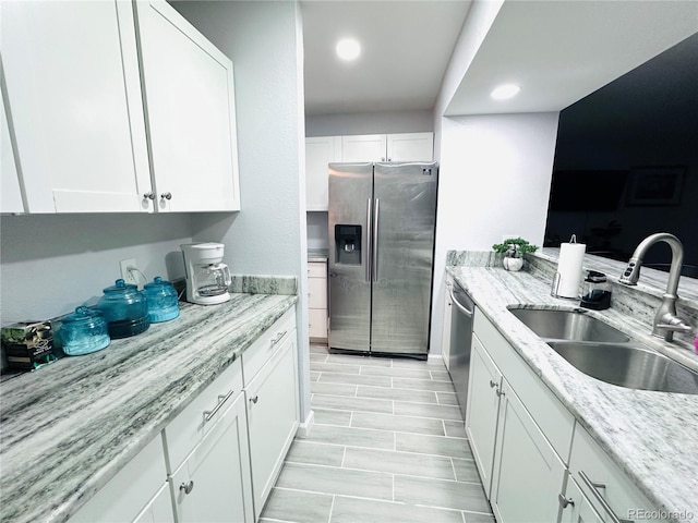 kitchen with stainless steel appliances, a sink, recessed lighting, white cabinetry, and light stone countertops